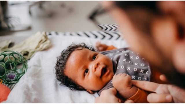a baby holding their parent's finger while looking into their eyes and smiling