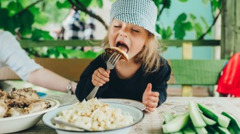 A little girl with a plate of cucumbers in front of her in the hopes that she'll eat veggies
