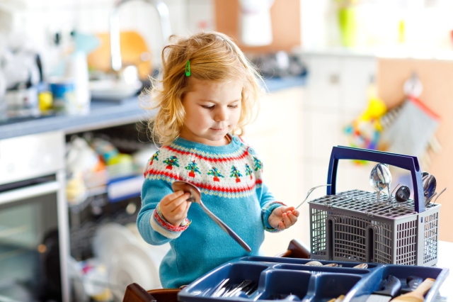 A girl in blue sweater helps load the dishwasher