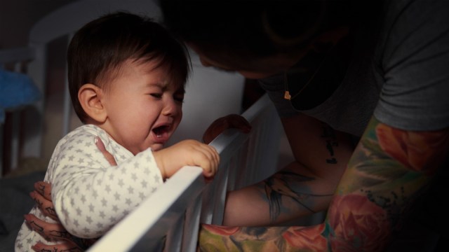 a toddler standing in their crib crying at night being comforted by a parent after a toddler nightmare