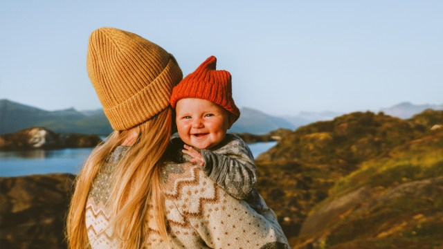 a mom who wanted to travel with baby standing in the mountains with her infant, both wearing beanie hats